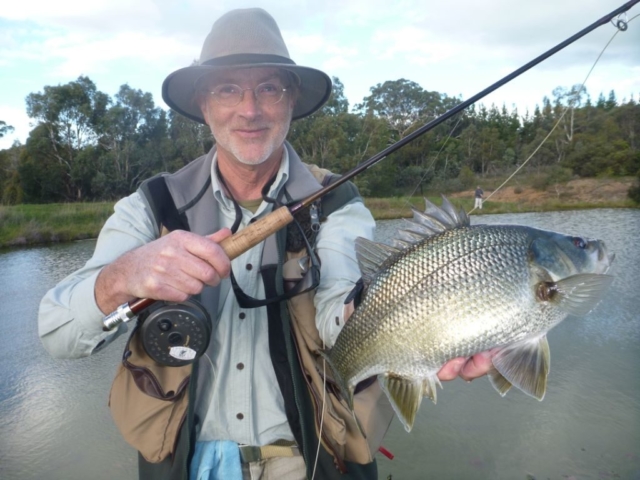 A man holding a big Bass by the lake