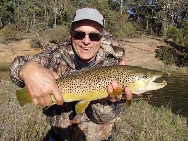 A man in camo gear with his big brown trout