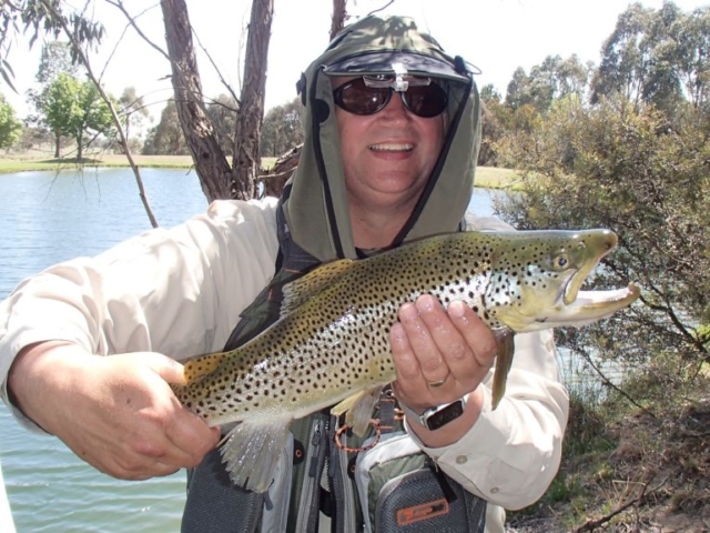 A man with his beautiful brown trout caught in an overgrown area