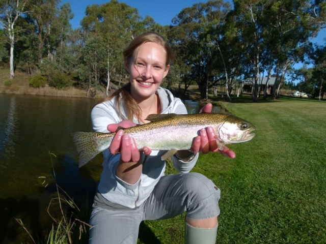 A young lady beside the waters edge with her pretty rainbow trout